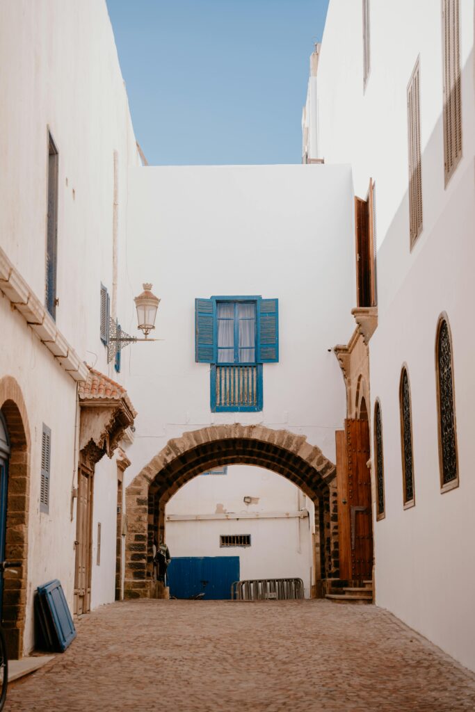 Essaouira Unveiled: A Coastal Odyssey - Day Trip from Marrakech to the Ancient Mogador City 4 Explore a serene alleyway in Essaouira with iconic white walls and vibrant blue shutters.