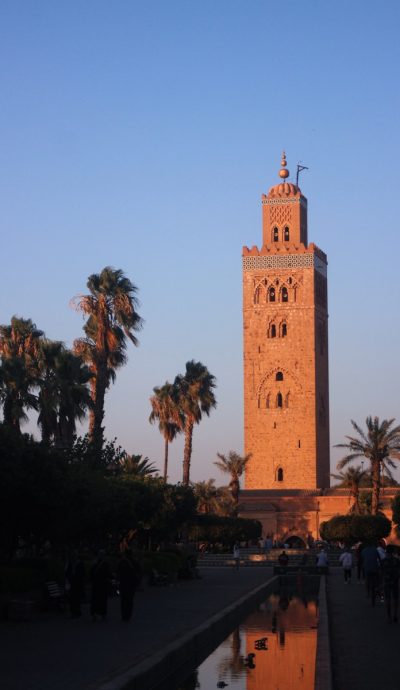 a tall tower with a clock with Koutoubia Mosque in the background