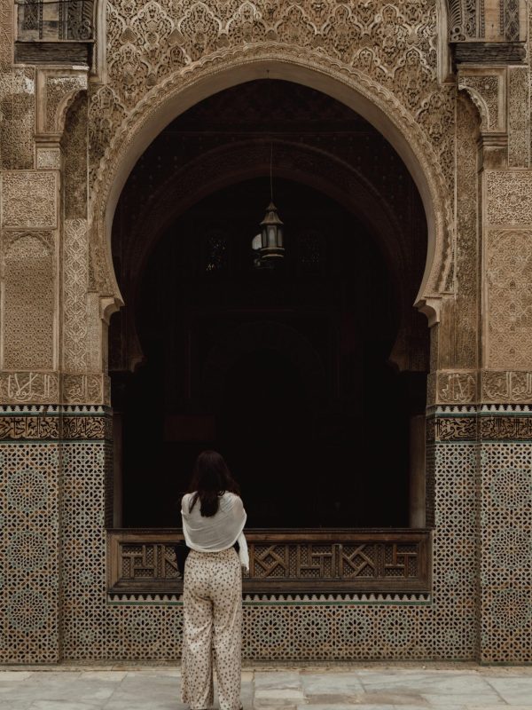 A woman stands in front of a beautifully intricate mosque arch in Fes, Morocco.