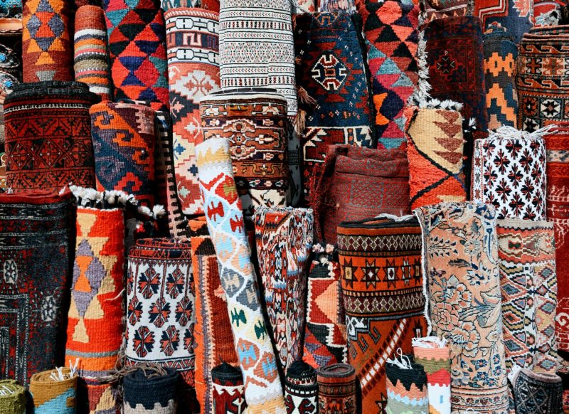 A colorful array of traditional rugs with intricate patterns at a market stall.moroccan rug​