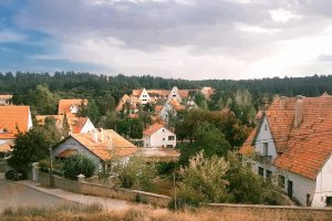 white and brown concrete house surrounded by green trees under white clouds during daytime