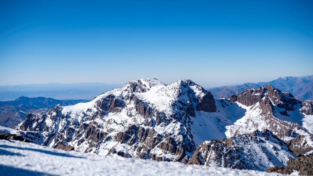 A snow covered mountain with a blue sky in the background.does it snow in morocco​
