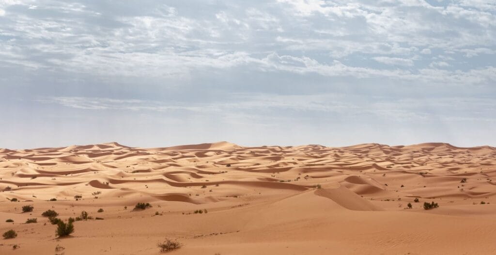 Expansive sand dunes stretch under a cloudy sky in the Algerian Sahara Desert.August Weather in Morocco