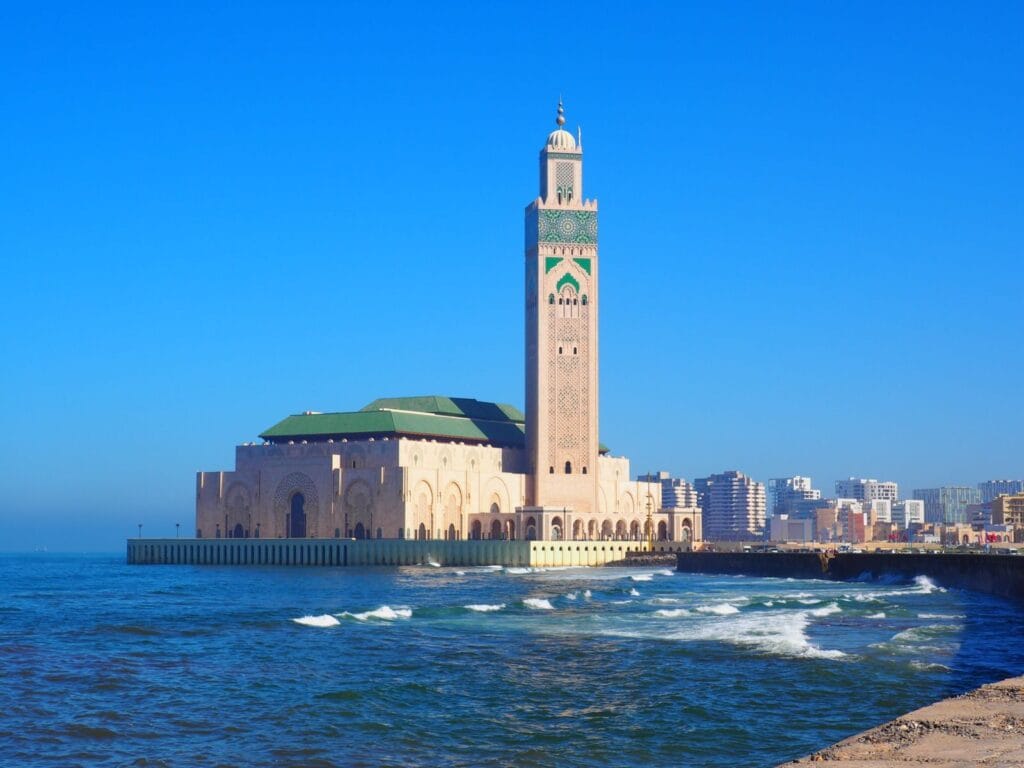 Hassan II Mosque in Casablanca against a vibrant blue sky and ocean waves.weather in morocco december