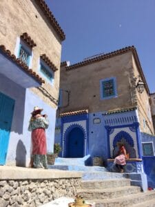 woman sitting in front of blue, moroccan people, concrete house