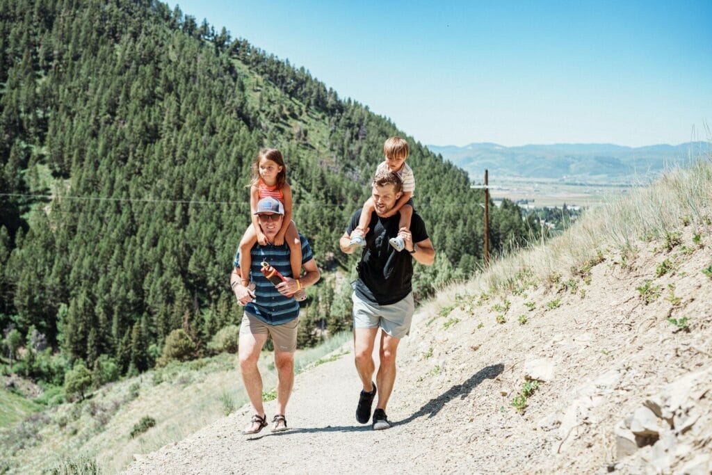 Two fathers carrying children on shoulders on a mountain path.Morocco in May weather