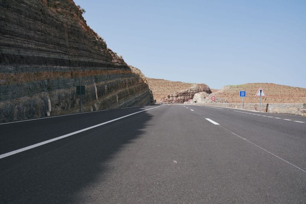 A deserted road cutting through rocky, arid landscapes under a clear sky.Marrakech Casablanca distance