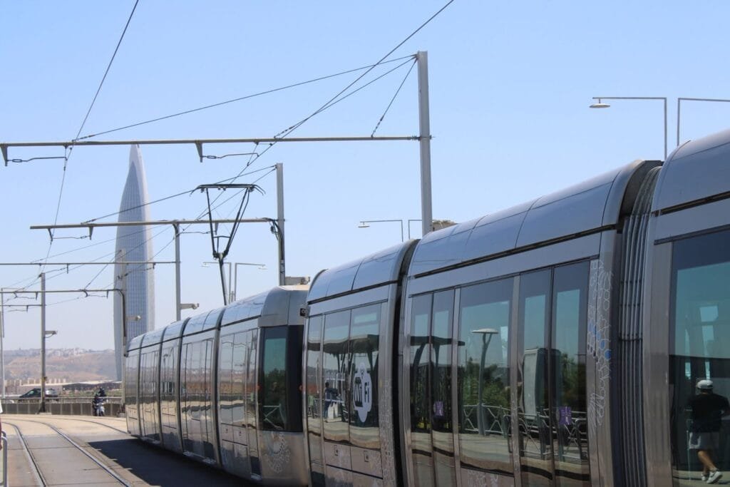 View of a modern tramway in Rabat with a distinctive tower in the background under clear blue skies.Marrakech Casablanca distance